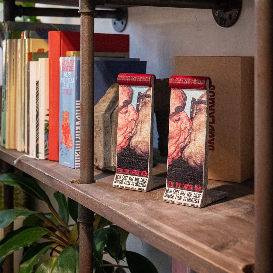 Two BRUDERKUSS Wall Pieces standing on a wooden bookshelf next to books